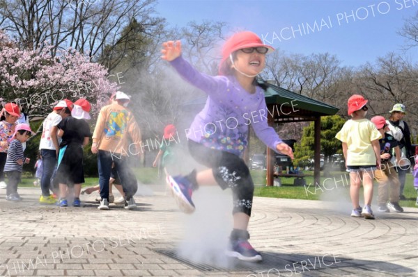 開花したサクラを背にミスト噴水で遊ぶ園児たち（２６日、午前１０時１５分ごろ、音更町役場前で。金野和彦撮影）