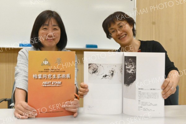 同窓生芸術展の作品集を手にする（左から）三浦尚代記念事業部副部長と高橋満紀子教諭。多分野の作家５１人の作品を収めている