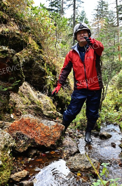 北海道石の露頭を背に解説する石橋氏。下の茶色い岩はオパールが地表で形成されたことを示す植物の化石