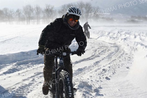 風が強く雪が舞う中で雪上ファットバイクを体験する参加者