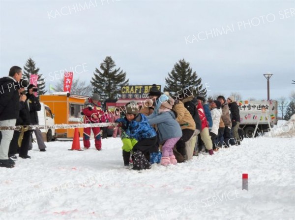 雪上で力一杯綱を引く参加者たち