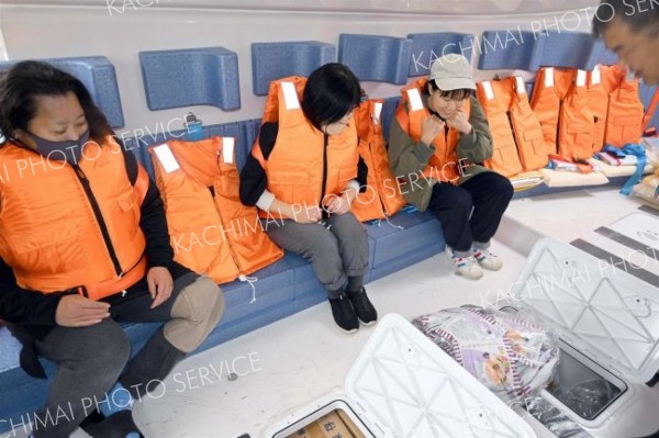 救命胴衣を試着し、座席に座りながら船底に保管されている備蓄食料を確認する住民