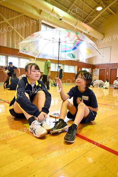 完成した傘を掲げる児童と一緒に笠に入る幕別清陵高校の生徒