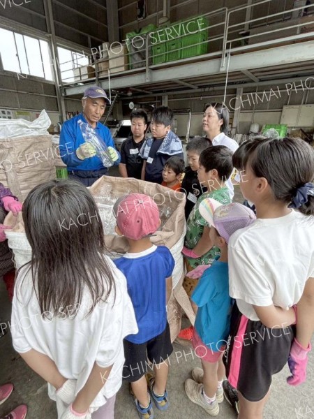 リサイクルセンターでゴミの分別方法に関する説明を真剣に聞く小学生たち