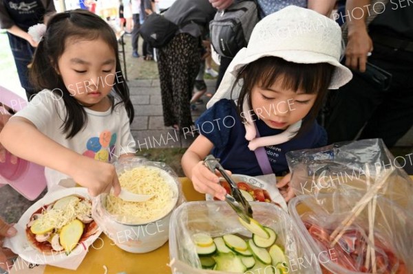 会場では食の体験コーナーも多数展開。思い思いの具を乗せて手作りピザを完成させる子どもたち（１日）