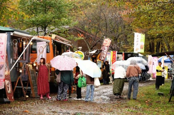 あいにくの雨の中、傘を差して会場内を回る来場者たち（１９日午前１１時半ごろ、助川かおる通信員撮影）