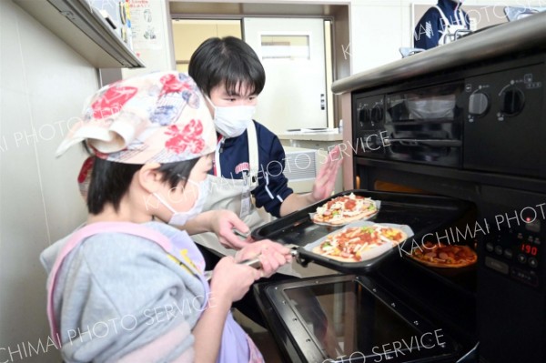 高校生に手伝ってもらいながらピザをオーブンに入れる子ども