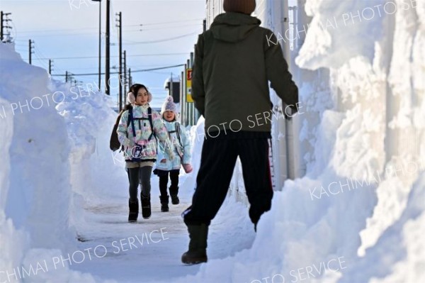 背丈以上の雪山に囲まれた歩道を歩く子ども（６日午前８時１５分ごろ、帯広市清流西１。塩原真撮影）