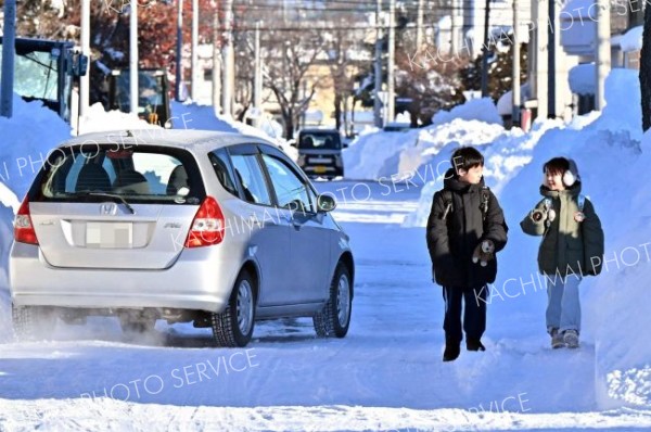 狭くなった道路脇を歩く児童と通行車両（７日午前８時ごろ、帯広市東７南９で。塩原真撮影）