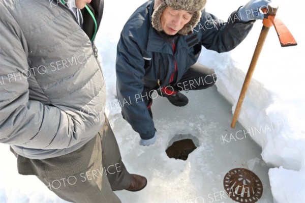 厚さ２５センチほどの氷の下にたまっていた水が排水されているのを確認する業者の男性