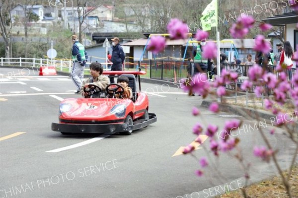 疾走　コース内の信号機や踏切などに注意しながら電動ゴーカートを楽しむ親子