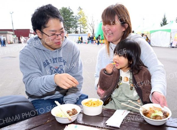 十勝の味覚を笑顔で楽しむ家族連れ。会場には香ばしい匂いが漂い、両手いっぱいに食べ物を持つ来場者の姿もあった
