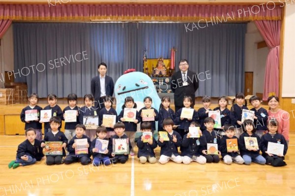 贈呈式に臨んだ関係者と贈られた絵本を手にする園児たち。後列左から
