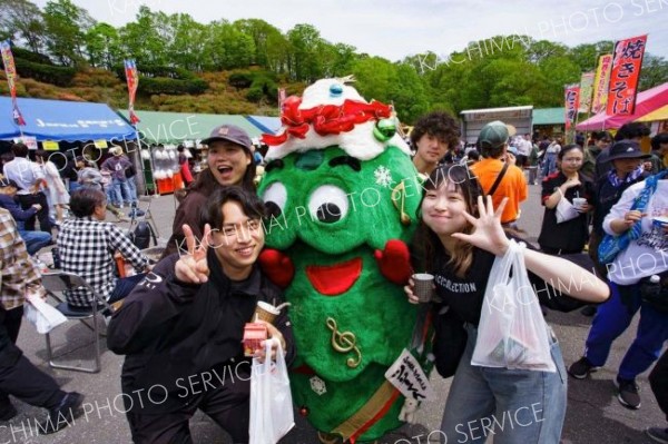 「五分咲き」のツツジをバックに、広尾サンタランドのマスコット「ツリー君」と記念写真を撮る来場者（石原秀樹通信員撮影）