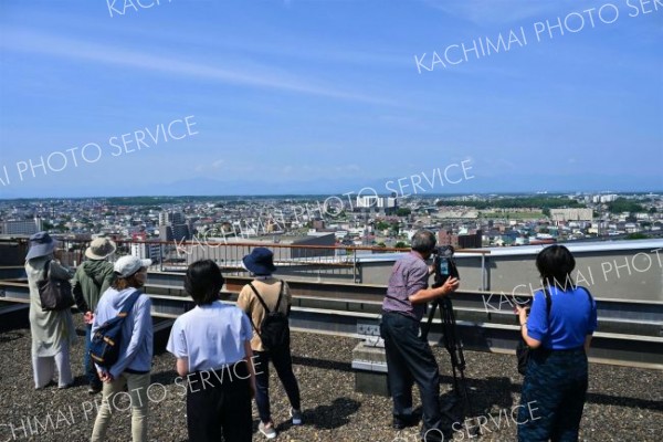 普段は立ち入ることができない帯広市役所屋上で日高山脈や市街地を眺める参加者（２５日午前９時半すぎ、塩原真撮影）