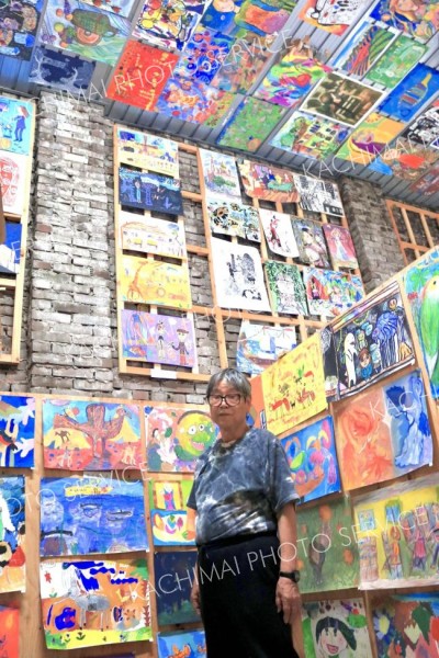 天井まで並ぶ子供たちの作品の前で来場を呼びかける