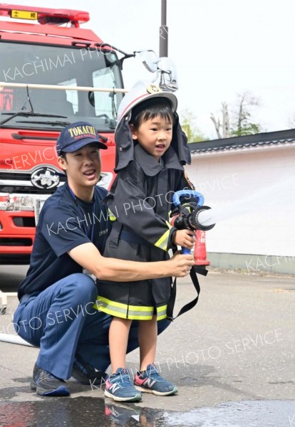防火服を身に着けて放水体験する子ども