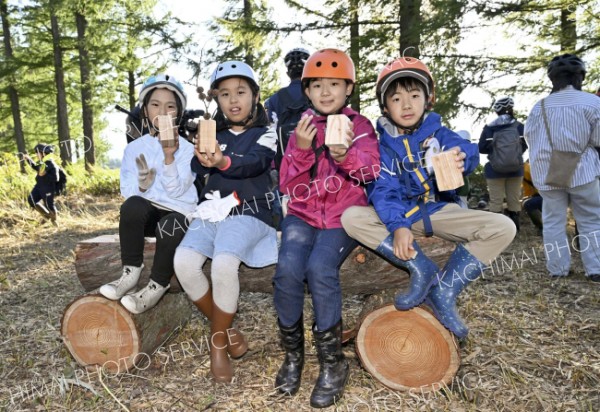 「座り心地はバツグン！」―。枯れ木で制作した急造のベンチに腰掛ける子どもたち、手には切り出した木で作った一輪挿しも。