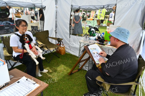 記念に１枚―。プロの似顔絵師に愛犬の似顔絵を描いてもらう来場者（１３日、「ドッグフレンドリーフェスタ」帯広市北愛国交流広場で。金野和彦撮影）