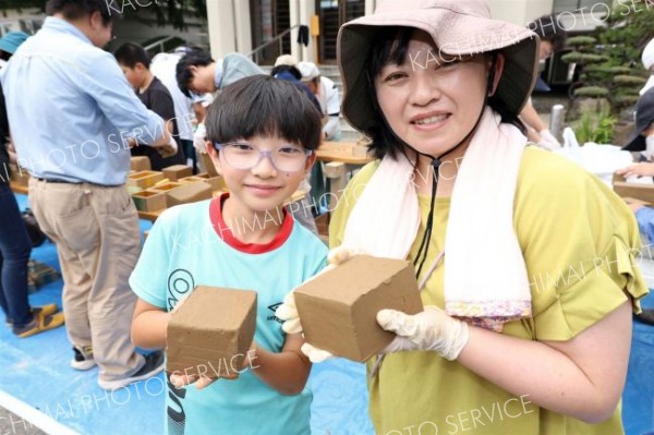 成形が完了したれんがを手に笑顔を見せる親子