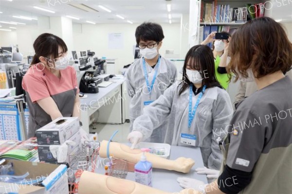 精巧な腕のダミーを使って採血の方法を学ぶ参加者