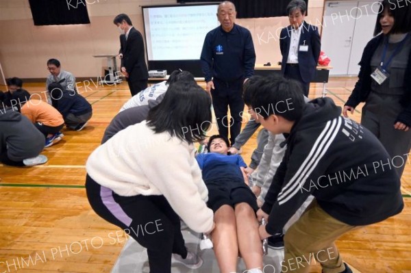 保温用アルミシートを用いた応急担架搬送を体験する子どもたち