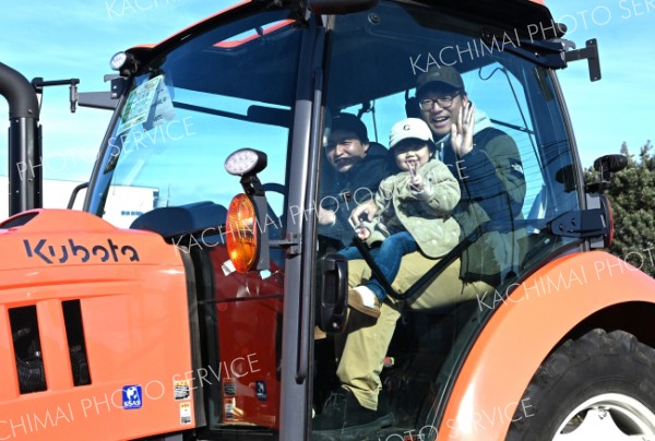 いってきまーす―。「めむろ大感謝祭２０２５」で開かれたトラクター体験試乗で運転席に座り手を振る親子（２３日、ＪＡめむろ特設会場で。須貝拓也撮影）
