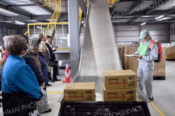 新たに完成した防災備蓄庫内で設備を解説する鈴木さん（右）と見学する町民ら