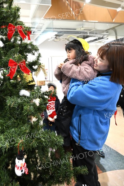 抱っこして―。先生に抱えられながらクリスマスツリーの上部に飾り付けを施す園児（３日、エスタ帯広東館で。須貝拓也撮影）