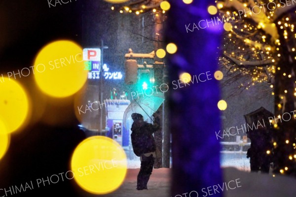 雪とイルミネーションに見とれ写真を撮る歩行者（１４日、帯広駅北口で。塩原真撮影）