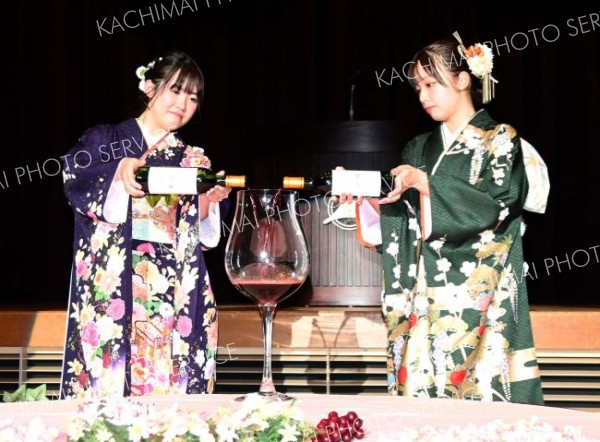 巨大グラスに生まれ年の十勝ワインを注ぐ大谷さん（左）と沼田さん