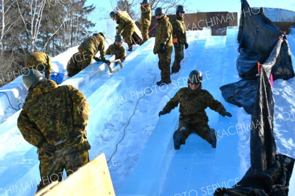 遊びじゃないよ―。「おびひろ氷まつり」の氷の滑り台を製作中の陸上自衛隊第５旅団の隊員が安全性の確認を兼ねて試験滑り（２２日、帯広市緑ケ丘公園で。金野和彦撮影）
