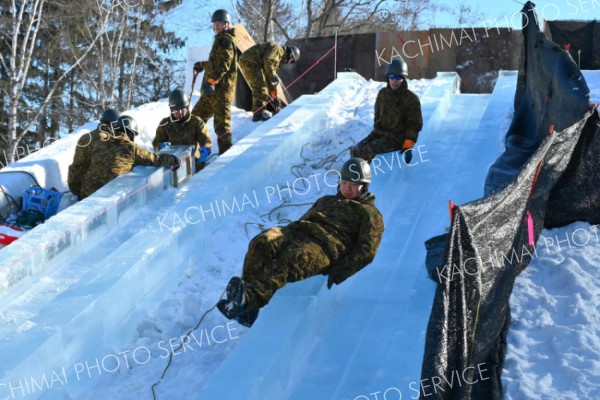 降下訓練！？―。「おびひろ氷まつり」の氷の滑り台造りが急ピッチで進む中、陸上自衛隊第５旅団の隊員たちが作業の効率化を図るために見せたパフォーマンス（２２日、帯広市緑ケ丘公園で。金野和彦撮影）