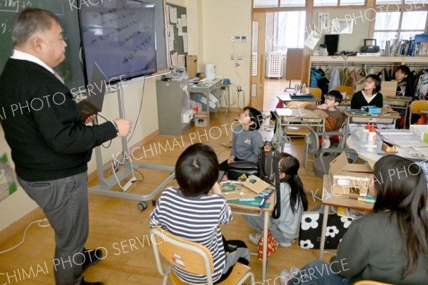 校歌の地上文字の編集前動画を児童らに紹介する田中校長（左）